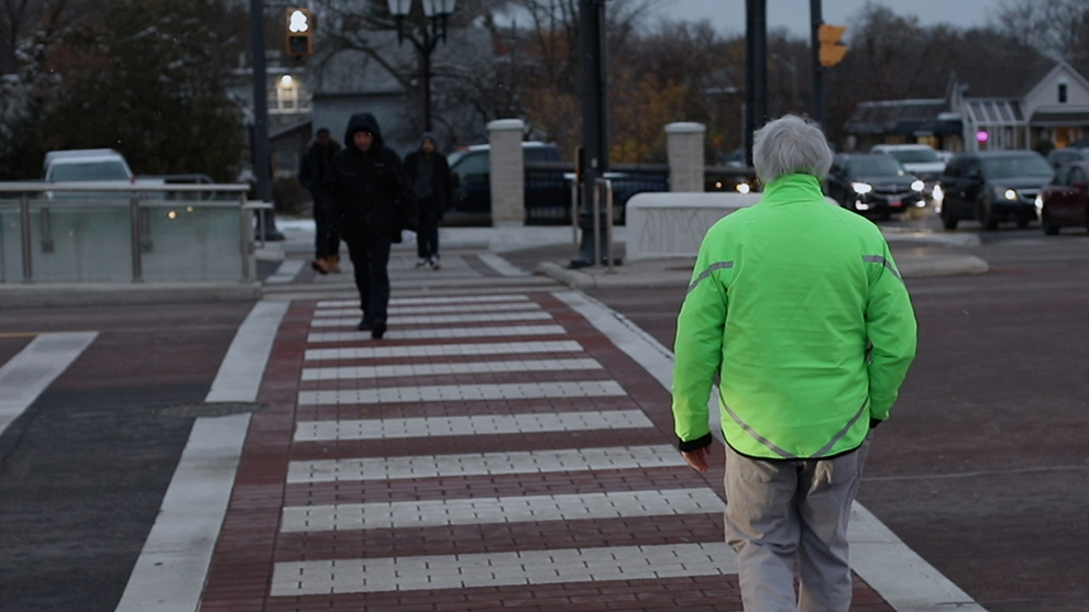 a man crossing the street at night in a bright green jacket