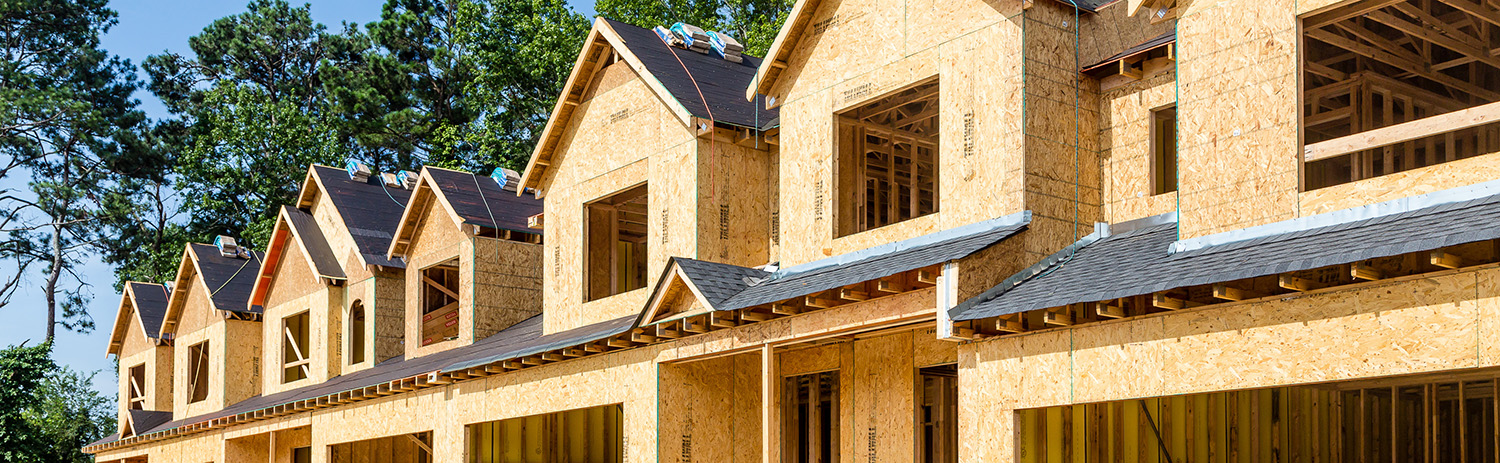 Row of timber-framed townhouses under construction with open garages and building materials in front.