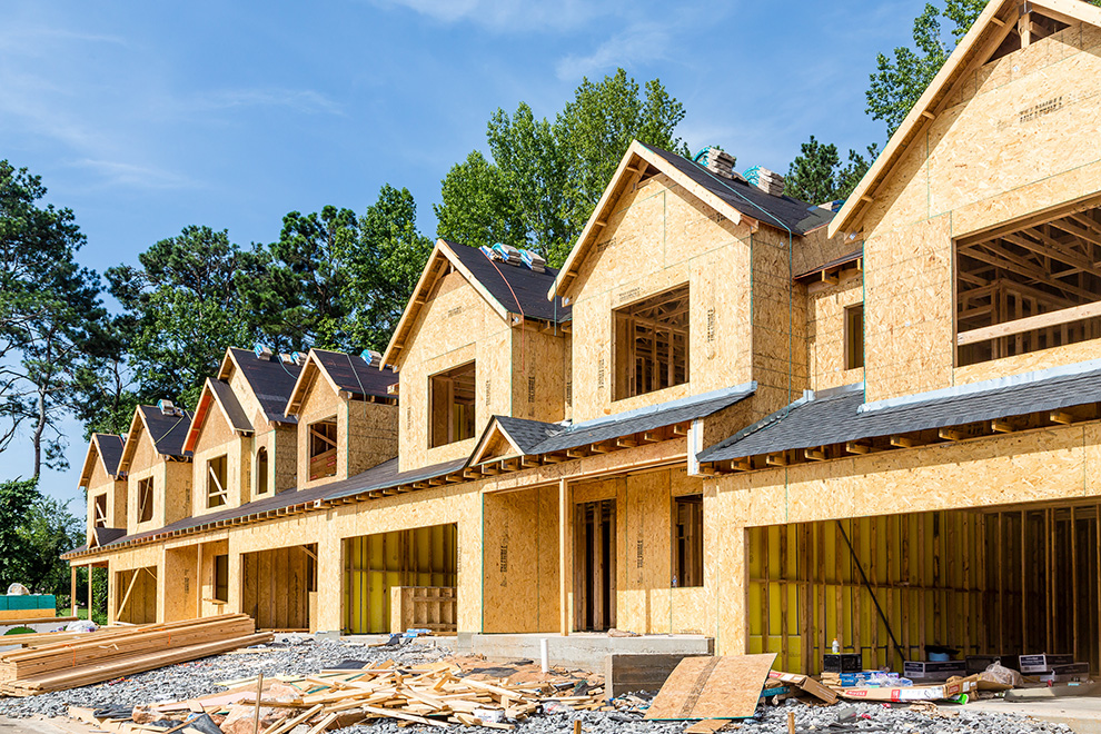 Row of timber-framed townhouses under construction with open garages and building materials in front.