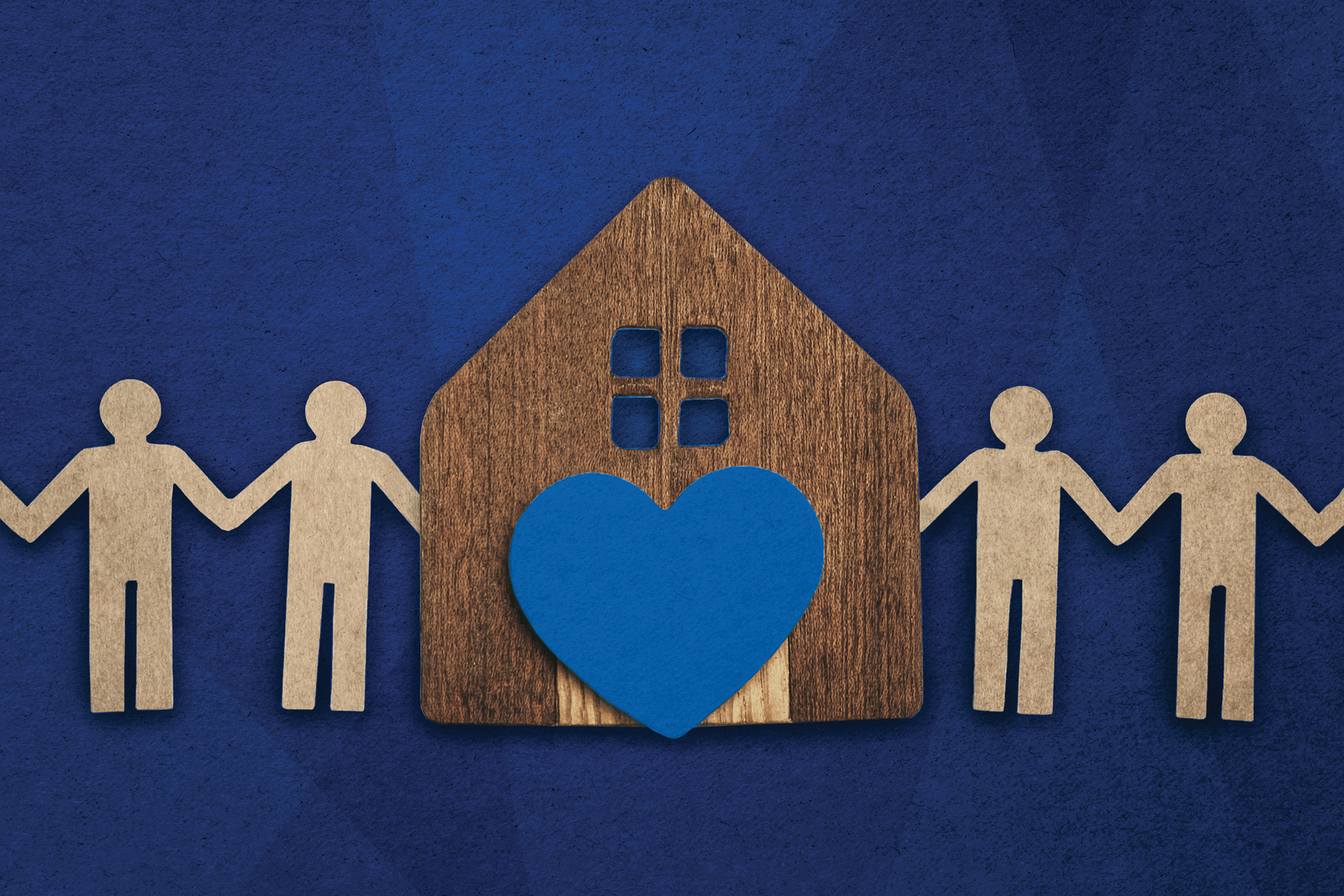 On a blue background, wooden cutouts of people around a wooden cutout of a house with a blue heart in front of it