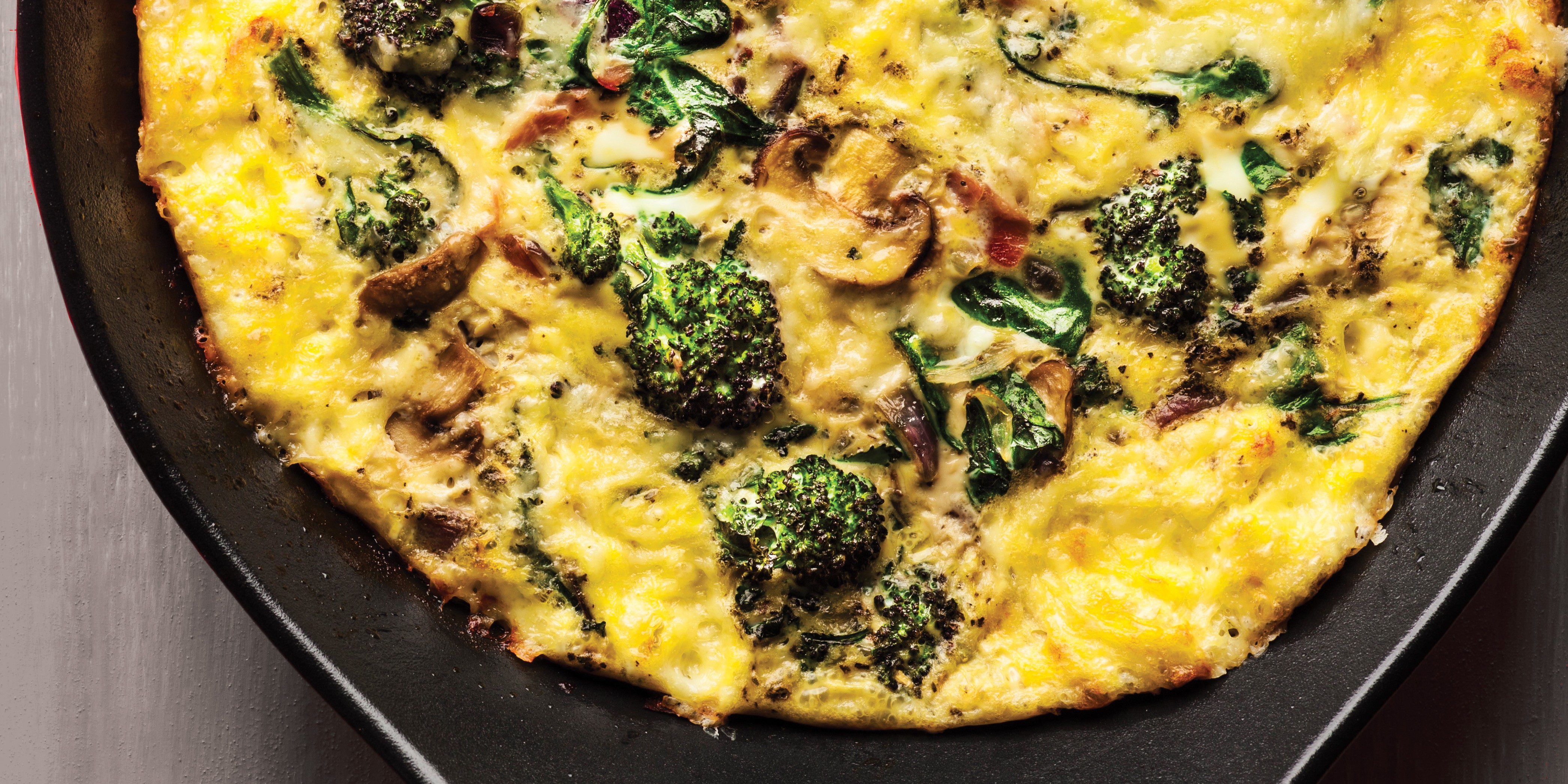 Vegetable frittata with broccoli, mushrooms, and leafy greens cooked in a skillet.