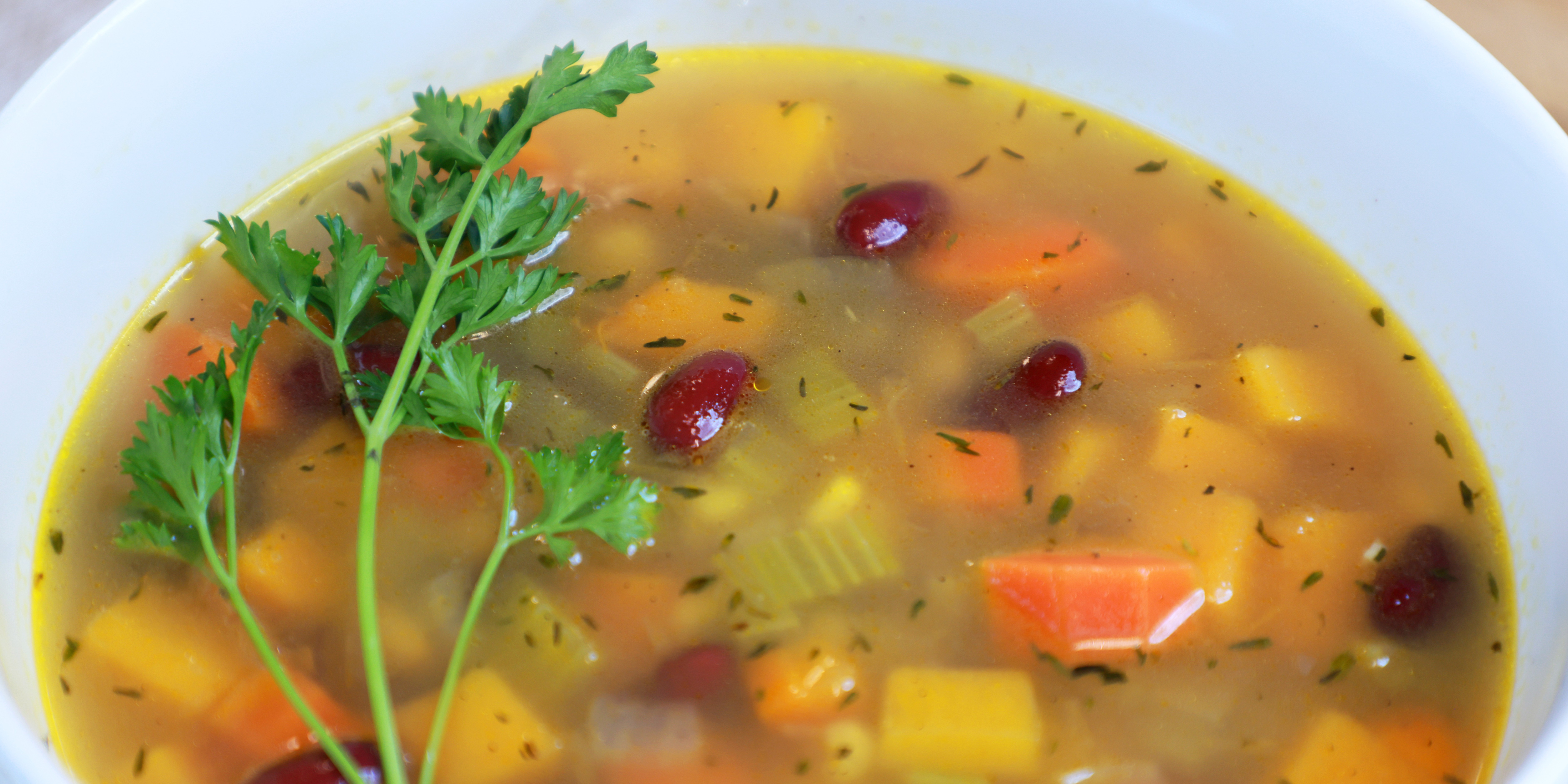 Bowl of vegetable soup with beans and fresh herbs on top.