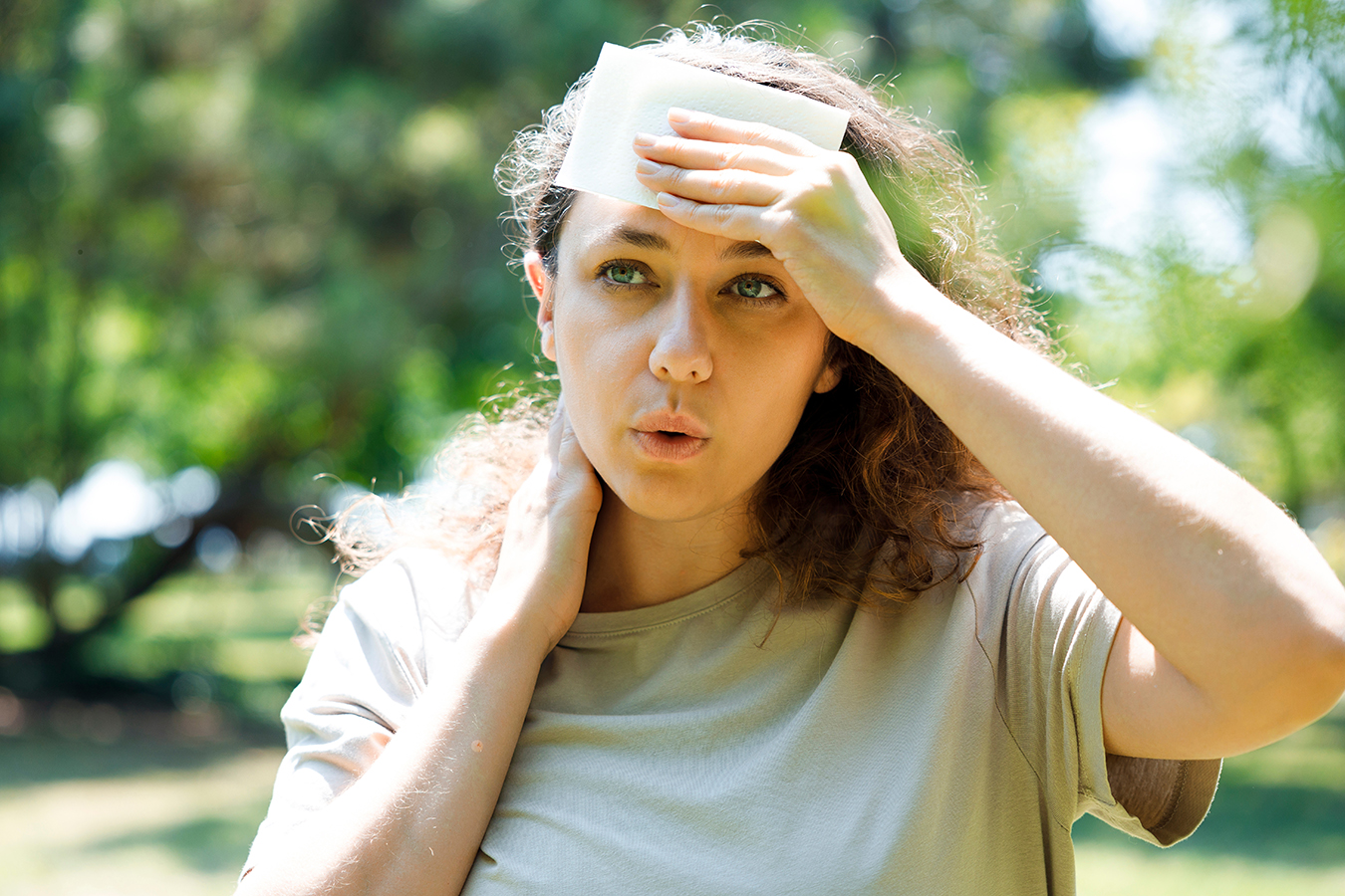Person cooling their forehead outdoors on a hot day.