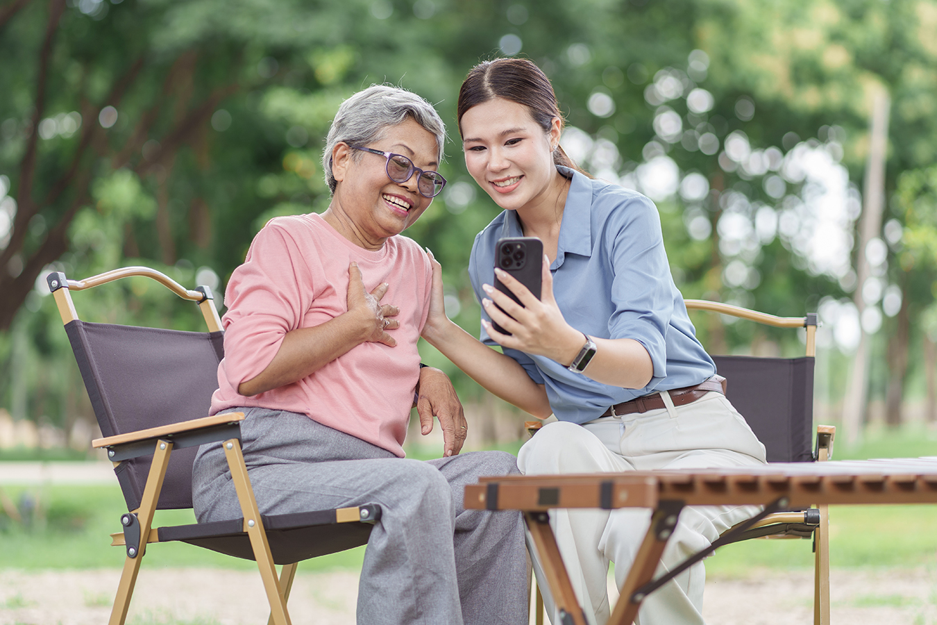An older adult and a younger adult sitting outside, looking at a smart phone together and smiling.