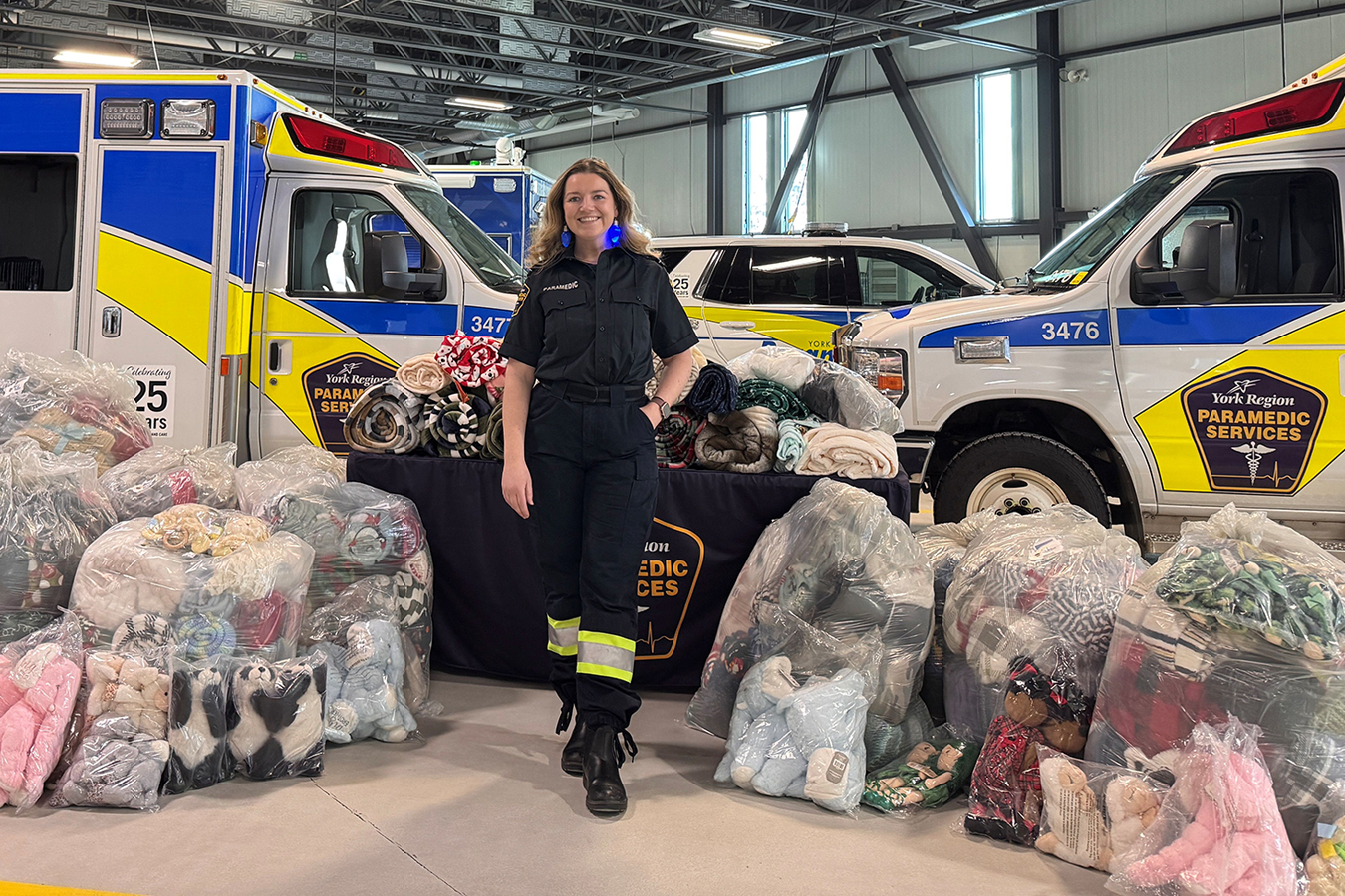 Paramedic stands between ambulances with bags of donated blankets and stuffed animals for York Region Paramedic Services.