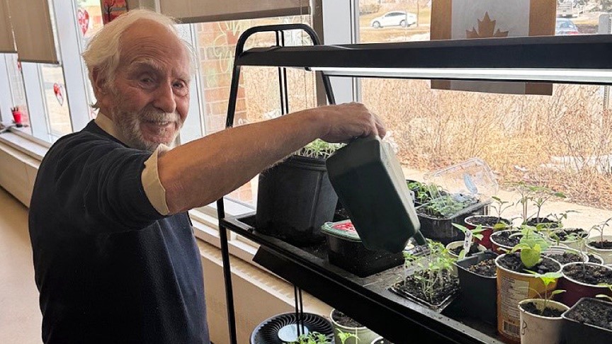 senior smiling at the camera watering seedlings
