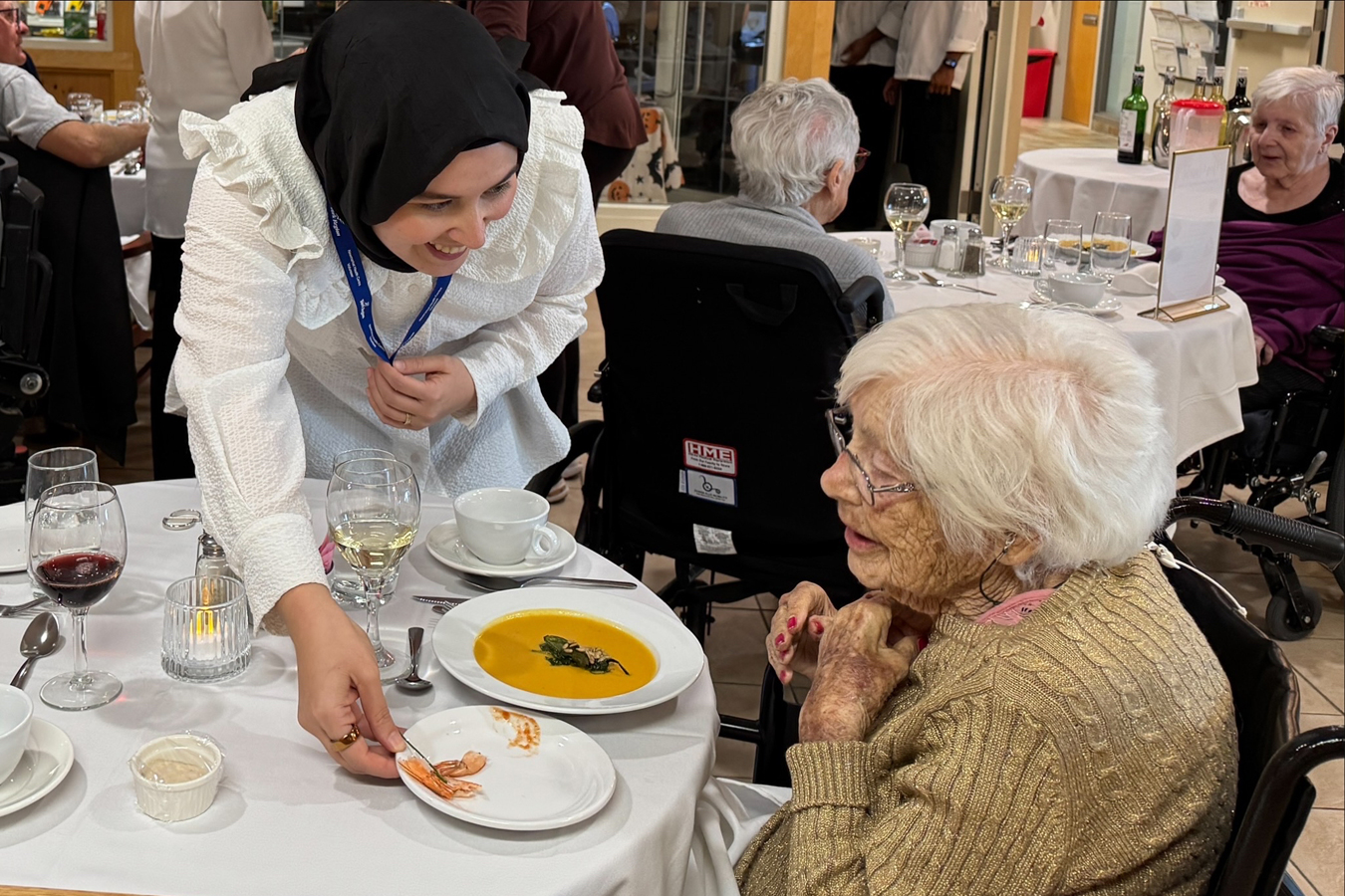 A York Region volunteer serves food to an older adult seated at a dining table in a community setting.