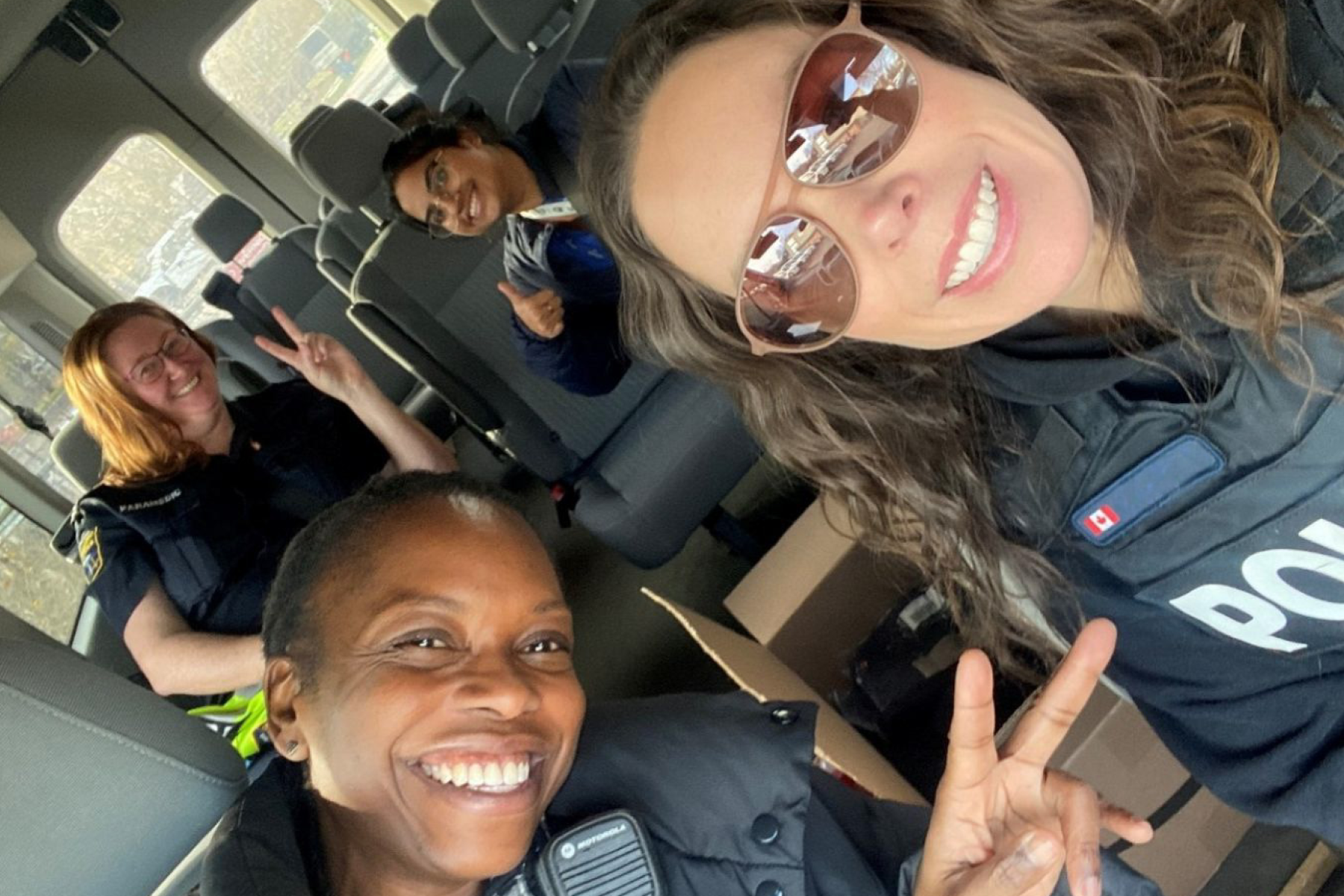 Inside a large passenger van, several individuals wearing uniforms are seated. The interior shows multiple rows of gray seats, and some people are making peace signs with their hands.