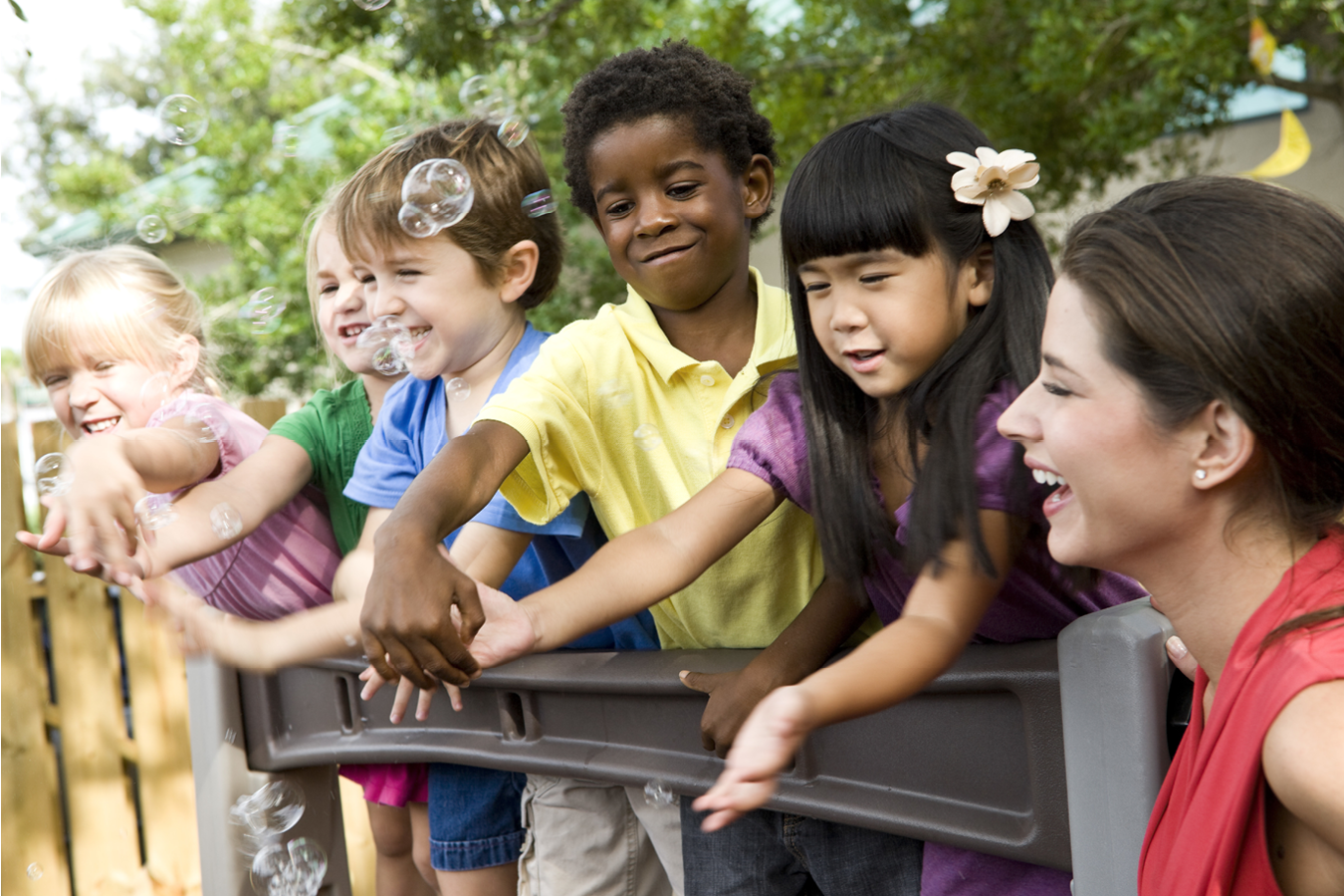 group of children with woman reaching for bubbles on outdoor play equipment