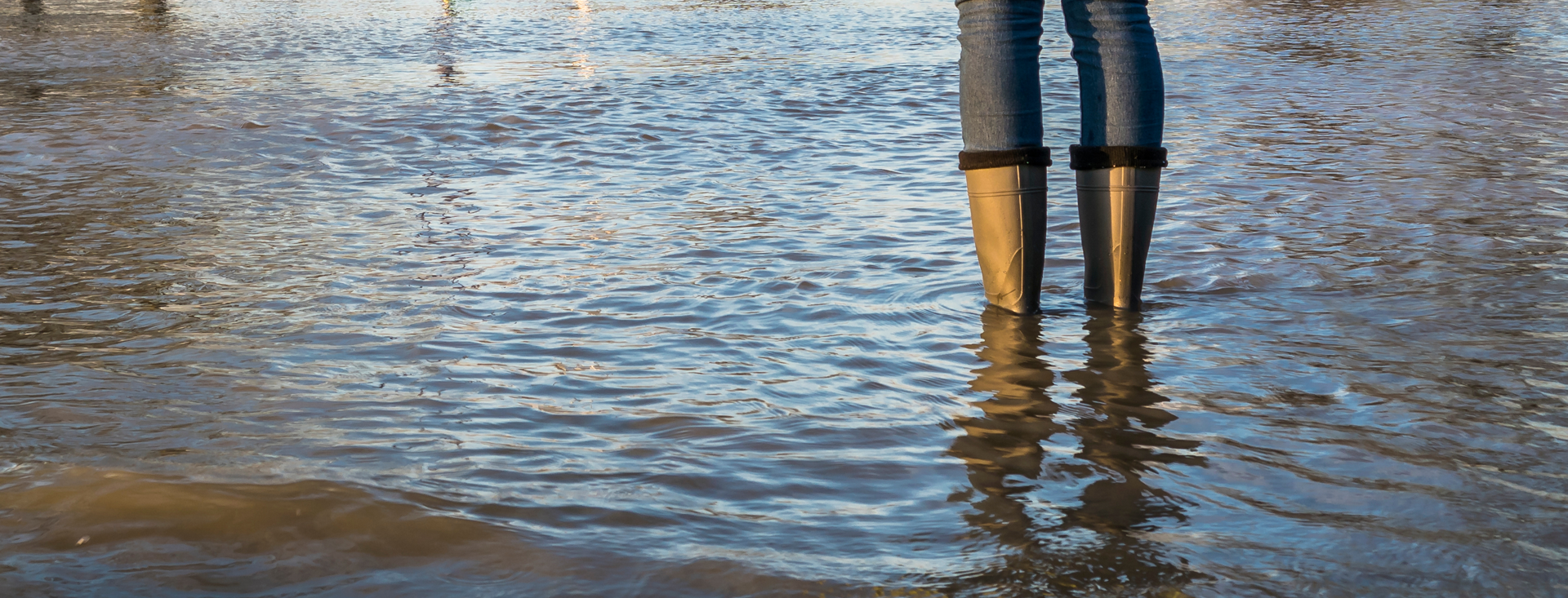 Photo of flooded street with a person standing in the water with rain boots
