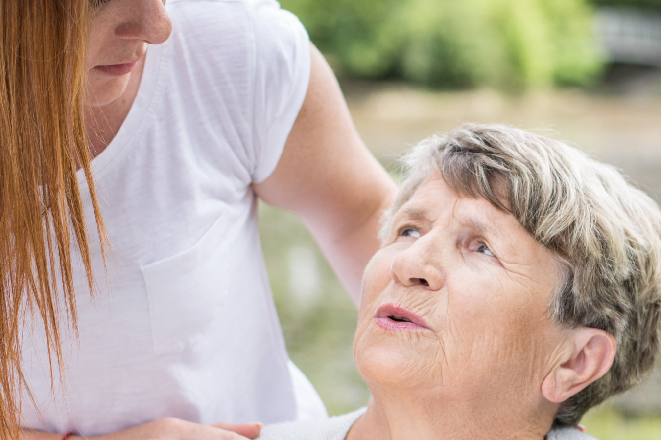 A distressed elderly person looking up at a younger person who is holding their shoulders