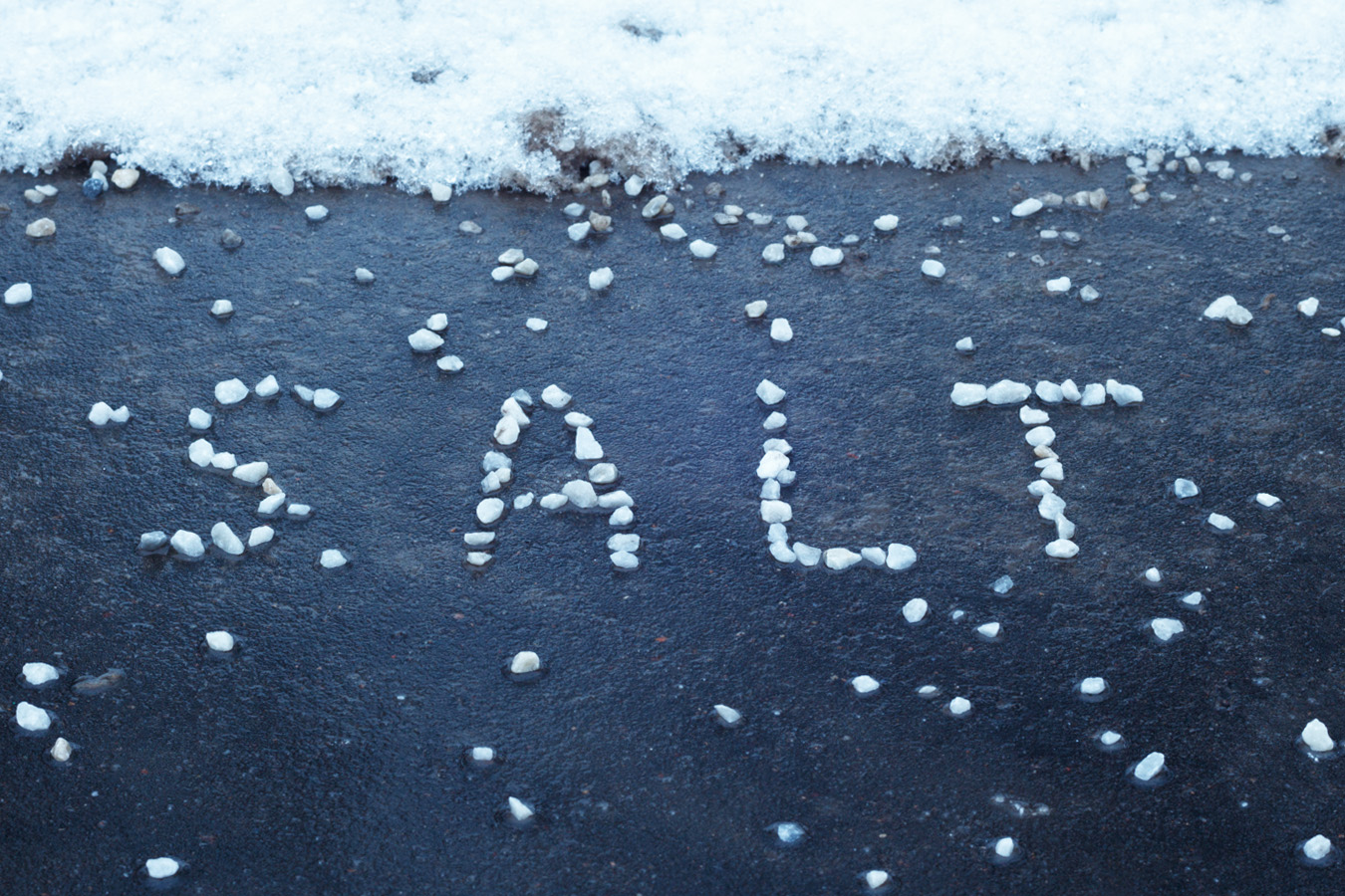 Salt chuncks, spelling the word SALT on pavement next to snow