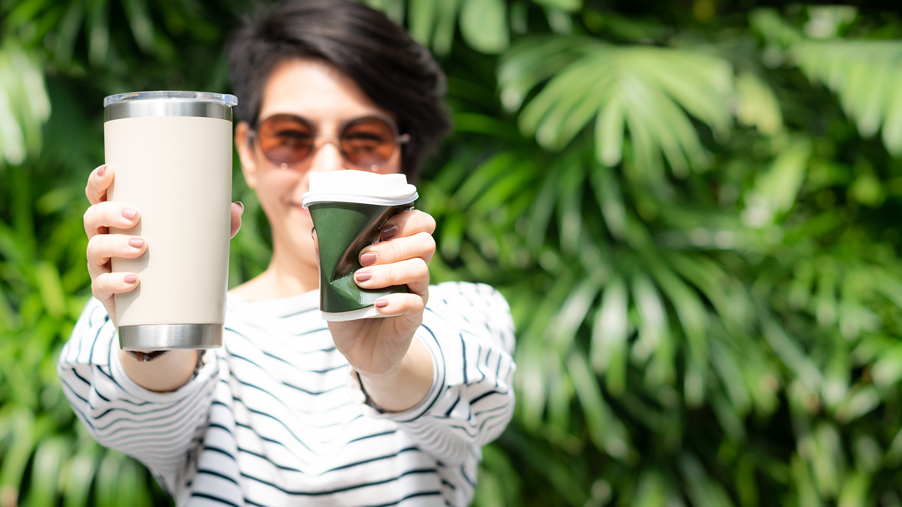 A women holding a reusable cup in one hand and squishing a disposable cup in her other hand