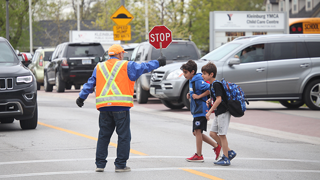 Crossing guard holding a stop sign to let two boys cross the street