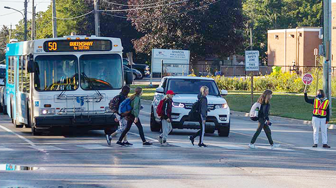 Children cross the street after school. the crossing guard helps the children.