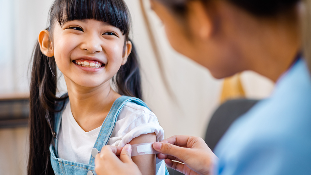 a young child having a bandaid applied by a nurse after receiving a vaccination in their arm