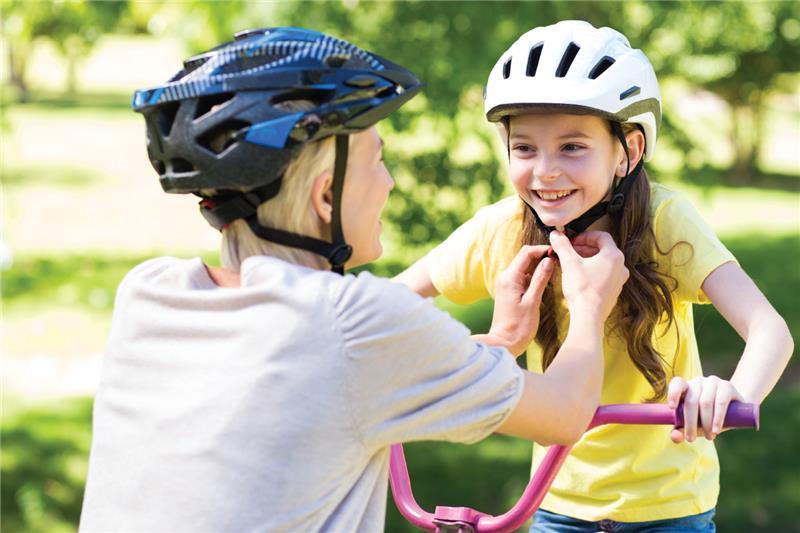 a women wearing a bike helmet tightening up a bike helmet on a young girl