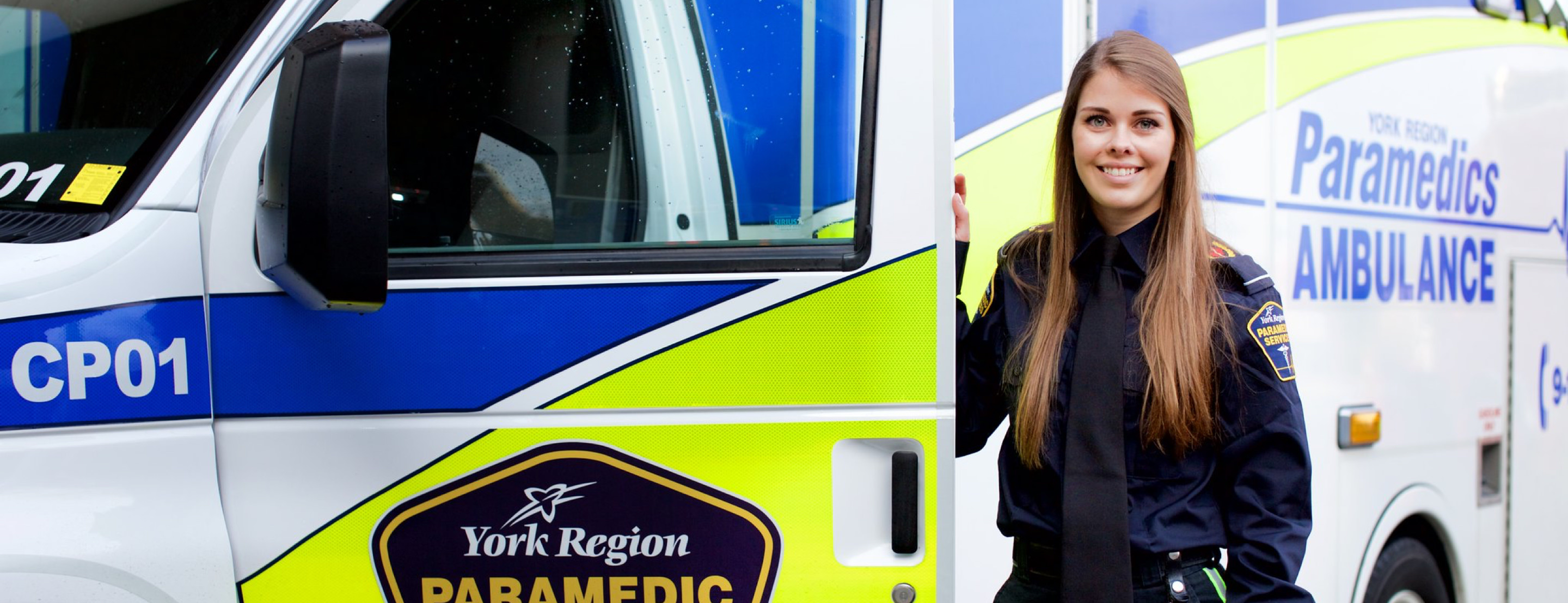Paramedic person standing next to paramedic vehicle smiling.