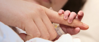 Baby hand holding finger of adult finger.