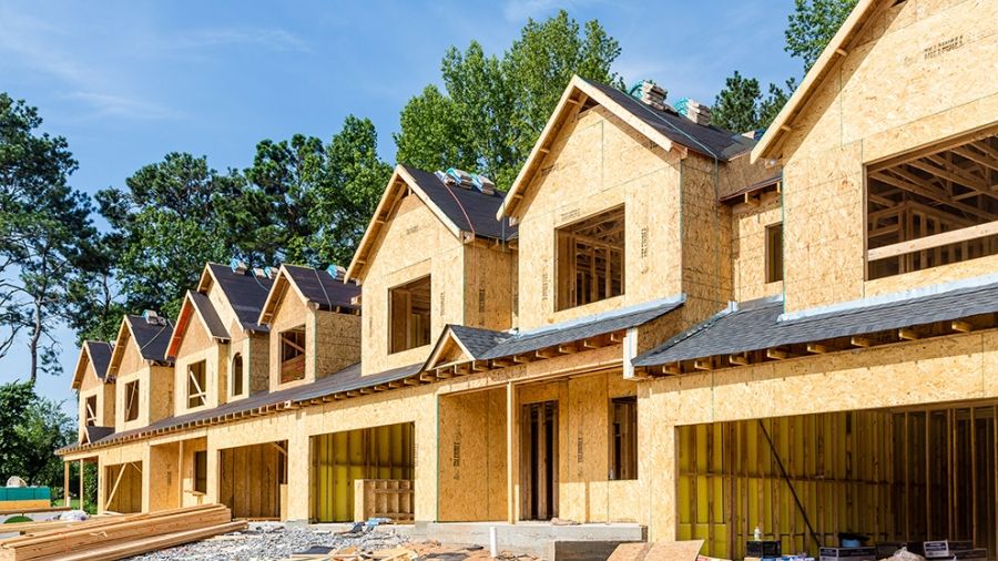 Row of timber-framed townhouses under construction with open garages and building materials in front.