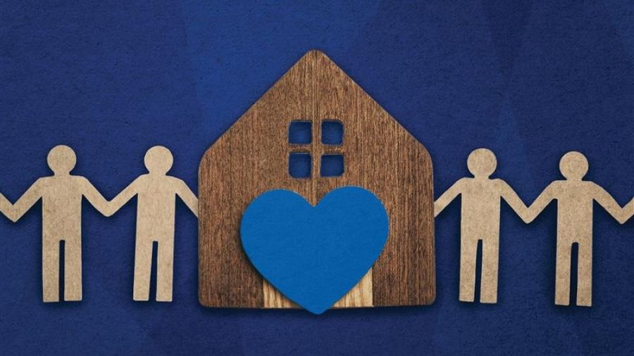 Wooden house with a blue heart, surrounded by paper‑cut people holding hands.