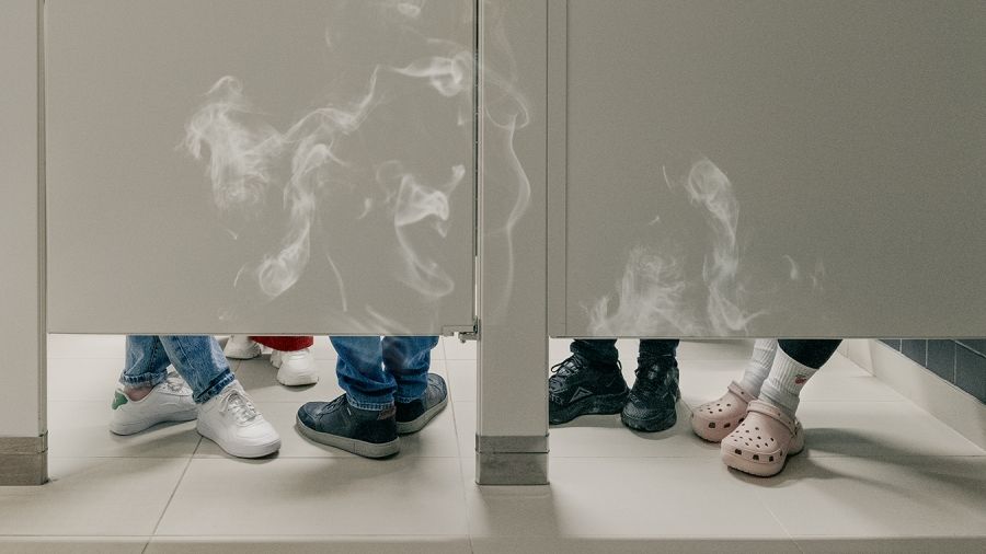 shoes under a bathroom stall with vape smoke rising