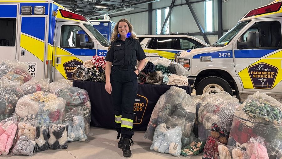 Paramedic stands between ambulances with bags of donated blankets and stuffed animals for York Region Paramedic Services.