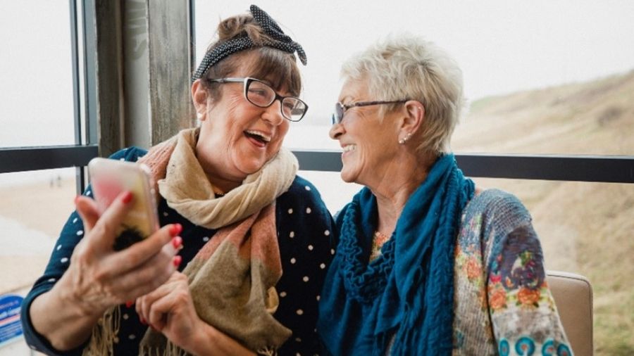 two seniors smiling while sharing a photo on a smart phone
