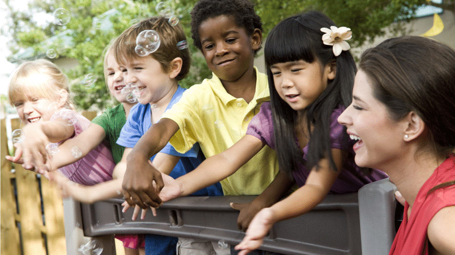 group of children with woman reaching for bubbles on outdoor play equipment