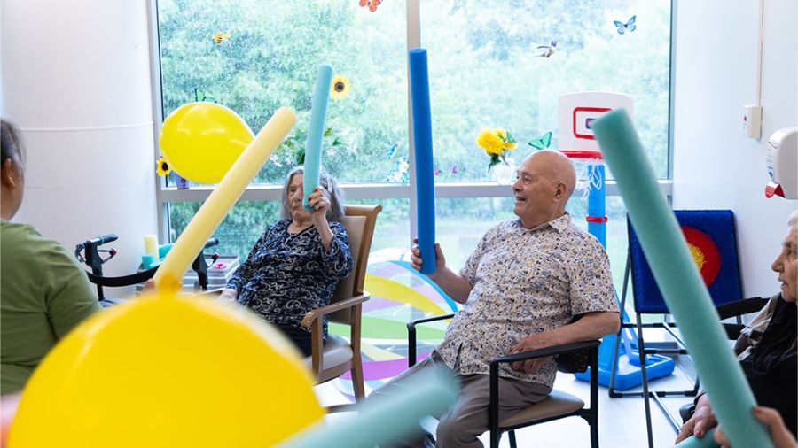 A group of seniors participate in a fun, active recreation program, using pool noodles and balloons to engage in a cooperative exercise activity.