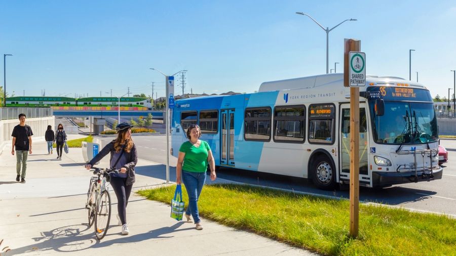 people walking and cycling on a shared pathway near a transit bus and a GO train