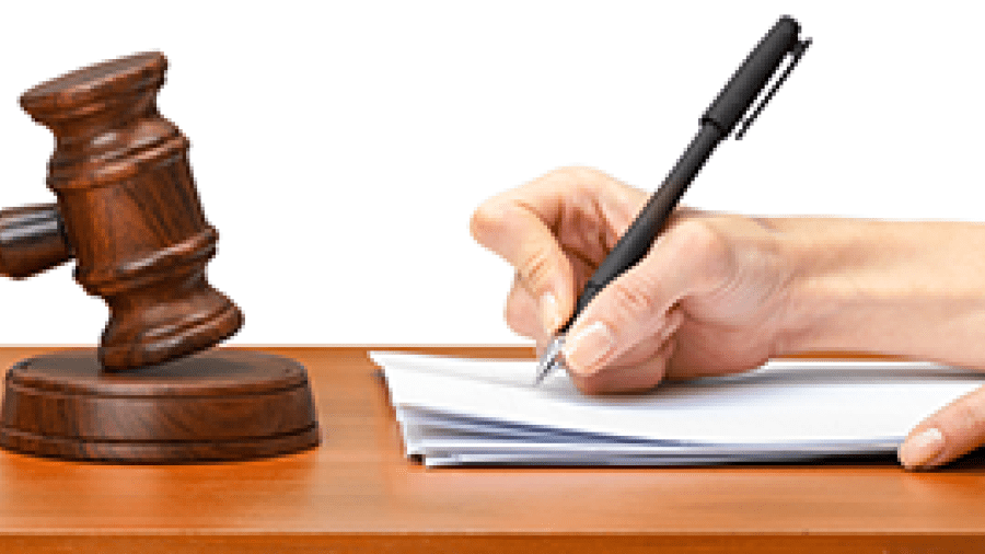 A judge writing at a desk also containing a gavel to indicate a conviction