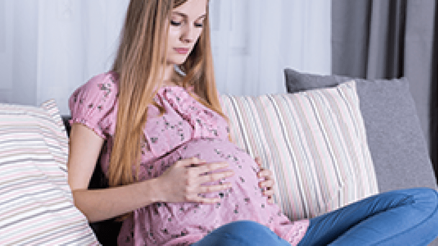 A young pregnant woman sitting on a sofa holding her belly