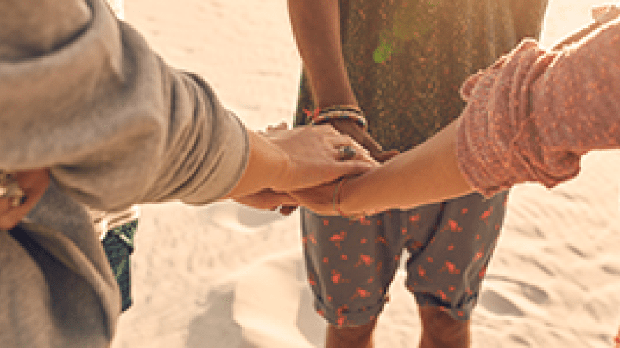 A group of young people standing on a beach, stacking their hands together