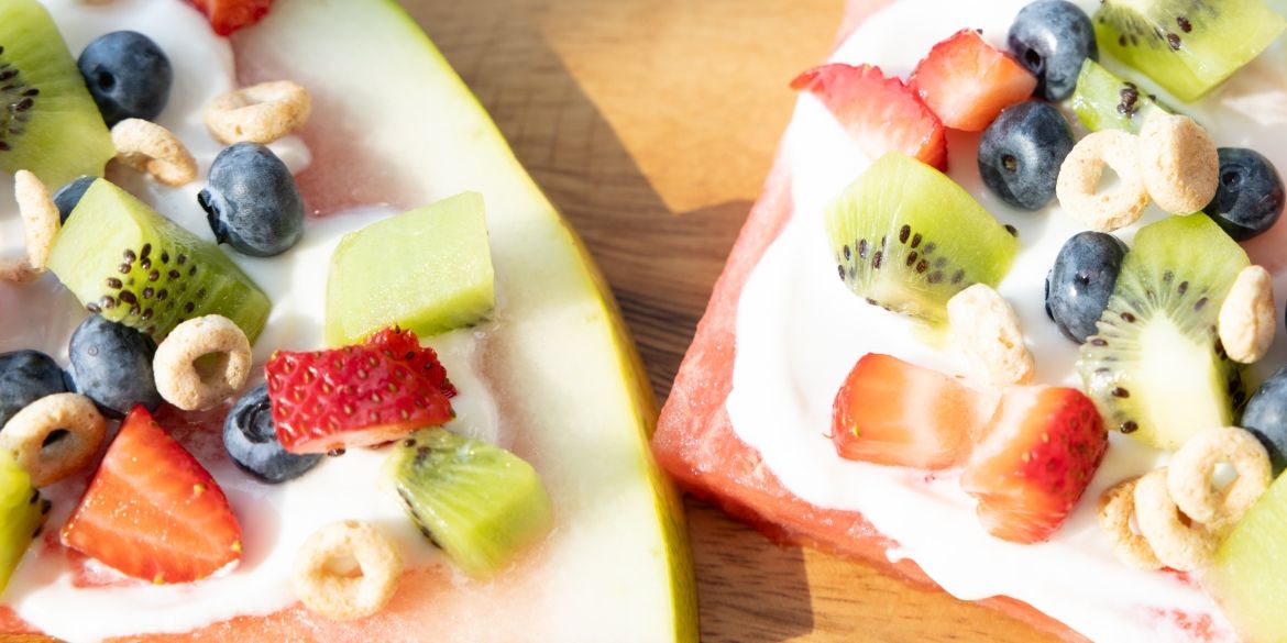 Watermelon slices topped with yogurt, fresh fruit, and cereal pieces.