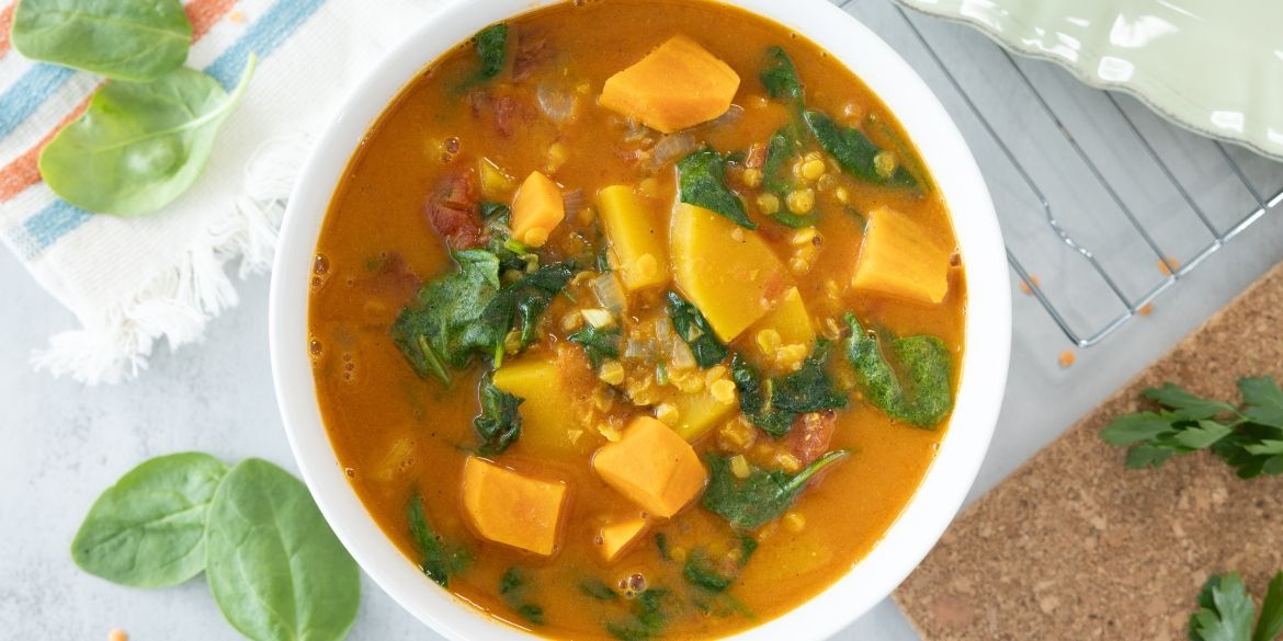 Bowl of sweet potato and lentil stew with spinach in a rich orange broth.
