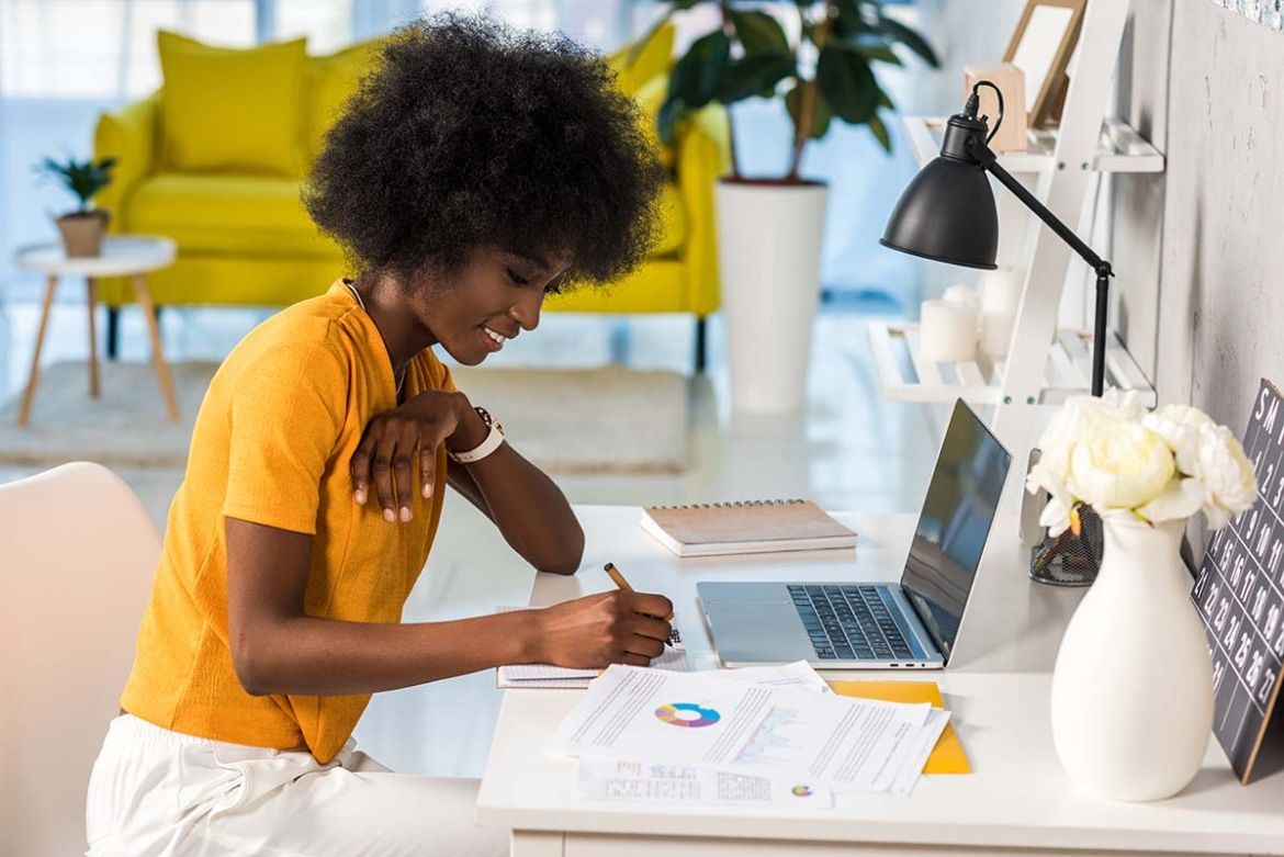 Woman writing on desk next to laptop