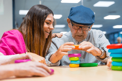 a caregiver watching a senior build a small tower out of colourful blocks