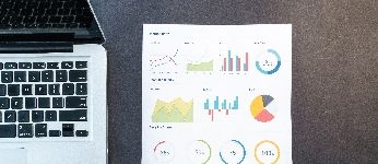 overhead of a laptop with a sheet of paper with charts on it