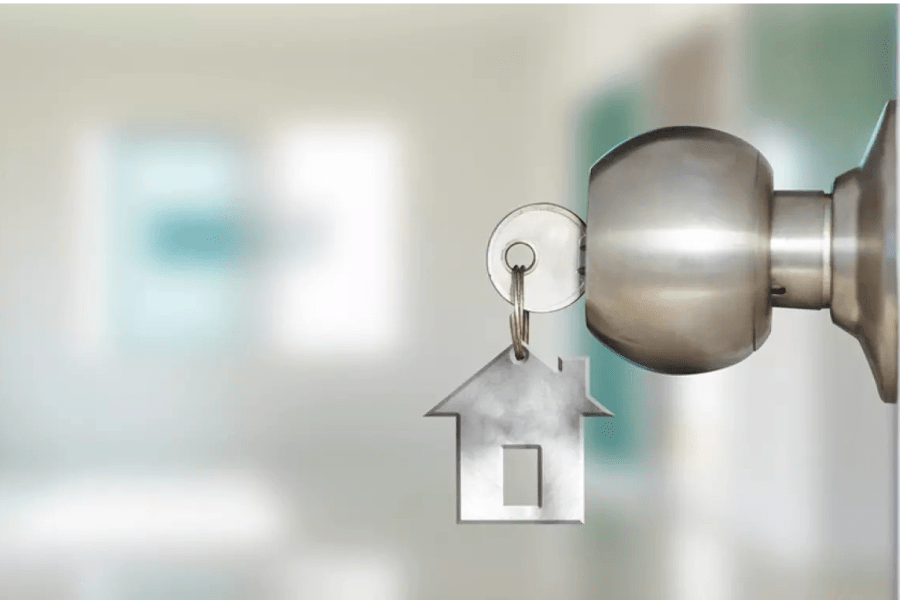 A door handle with a key in the lock and a keychain that looks like a home / Une poignée de porte avec une clé dans la serrure et un porte-clés qui ressemble à une maison
