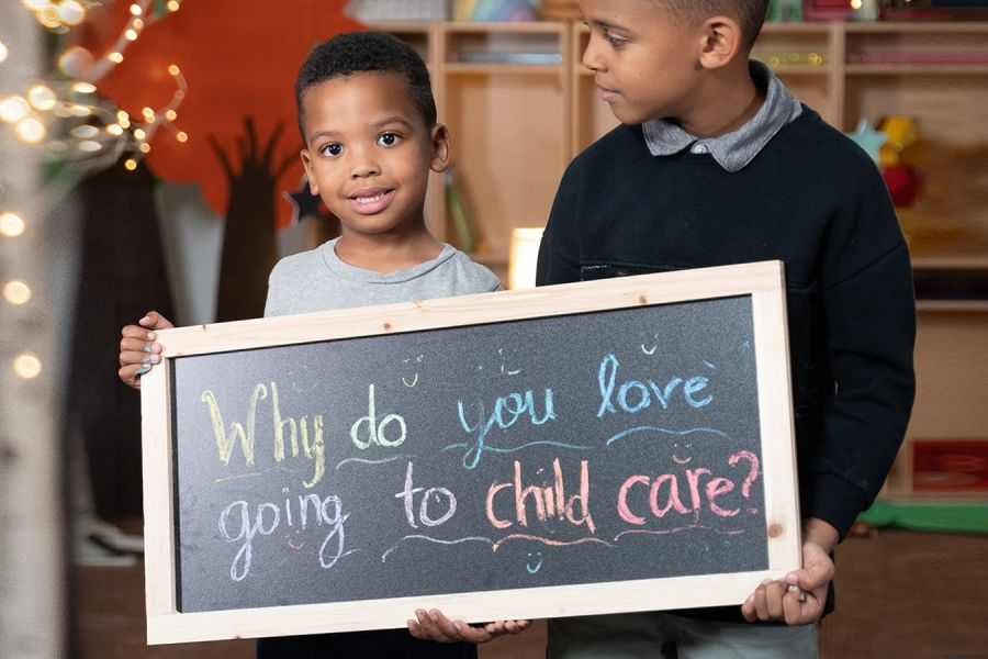 two children holding a sign saying "Why do you love going to child care?"