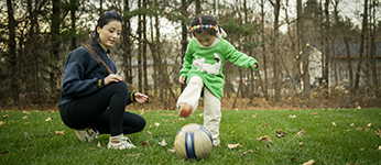 A young girl kicking a soccer ball while her mother watches