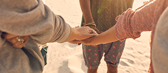 A group of young people standing on a beach, stacking their hands together