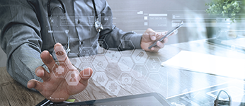 A doctor at a desk touching an electronic screen in front of him